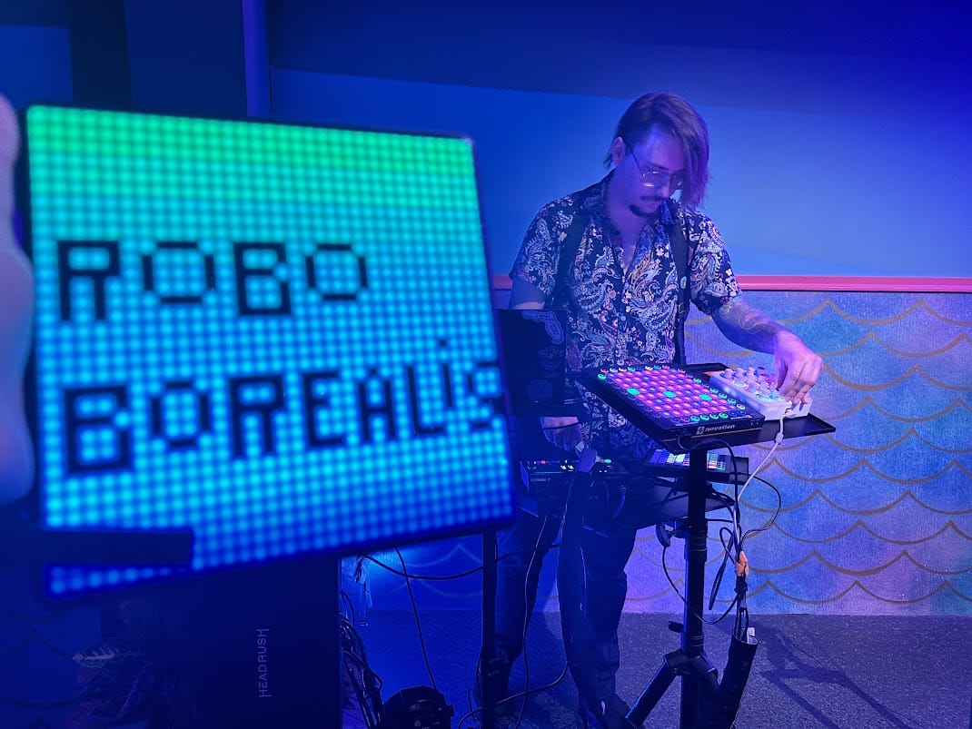 roboBOREALIS playing a live set at Floridarama in 2023, next to a glowing ROBO BOREALIS sign