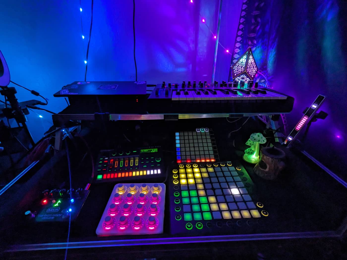 The roboBOREALIS home studio rig: synth, drum machine and pad controllers under blue and violet light